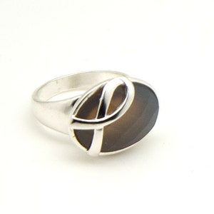 May include: A silver ring with a brown oval gemstone set in a silver swirl design.