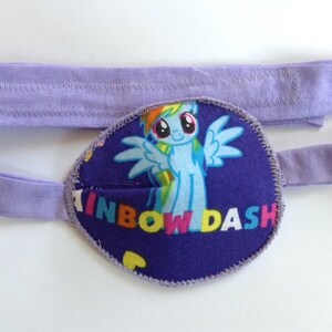 Può includere: Parche per l'occhio viola con un'immagine di Rainbow Dash di My Little Pony. Il cerotto ha uno sfondo viola con un arcobaleno e il testo "Rainbow Dash".