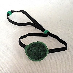 May include: A green eye patch with a black elastic strap and green beads. The eye patch is made of soft fabric.