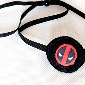 Könnte beinhalten: Schwarze Augenklappe mit elastischem Band und rotem Deadpool-Logo.