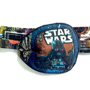 May include: A blue and black eye patch with a Star Wars comic book design featuring Darth Vader. The patch has a blue border and the text "STAR WARS" is printed in white.