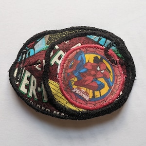 May include: Three round fabric patches with black stitching. The largest patch features a red and blue image of Spider-Man in a web design. The text "Spider-Man" is visible on the bottom of the patch.