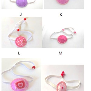 May include: Five eye patches with different patterns. The eye patches are pink, purple, and white with polka dots, hearts, and flowers. The eye patches are attached to white elastic bands with red beads.