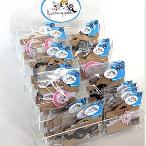 May include: A clear acrylic display case filled with various eye patches. The eye patches are packaged in clear plastic and attached to cardboard backing. The display case has a sign at the top with the text "Eye love my patch".