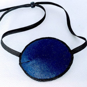 May include: A blue eye patch with a black elastic strap. The patch is made of soft fabric and is designed to cover one eye.