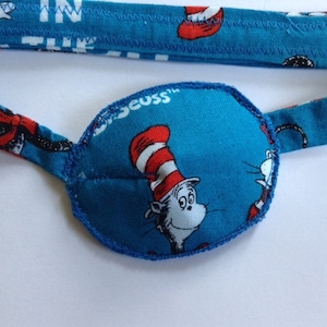 May include: A blue eye patch with a white and red cat wearing a hat with the words "The Cat in the Hat" on the strap.