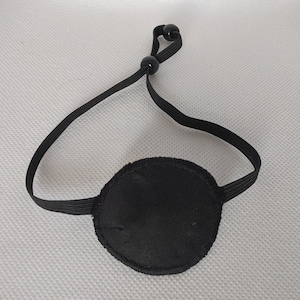 Puede incluir: Un parche para el ojo negro con una correa elástica. La correa tiene dos cuentas negras en el extremo.