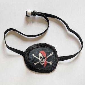 以下が含まれることがあります： 赤いバンダナが付いた、スカルとクロスボーンのデザインの黒い海賊の眼帯。パッチは、調整可能な白いビーズが付いた黒いゴムバンドに取り付けられています。コスチュームやテーマのあるイベントに最適なアクセサリーです。