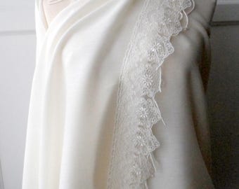 May include: Cream-coloured shawl draped over a mannequin. The shawl has a delicate lace trim along the edges, adding elegance. The fabric appears soft and flowing, suggesting a lightweight material. Suitable for special occasions.