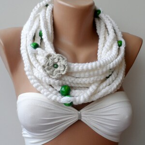 May include: White crocheted infinity scarf with green wooden beads and a crocheted flower accent.