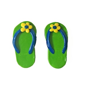 Könnte beinhalten: Ein Paar grüne Flip-Flops mit blauen Riemen und gelben Blumenverzierungen.