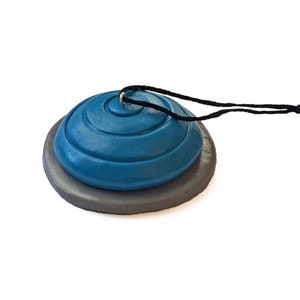 May include: A blue and gray ceramic ornament with a black string for hanging. The ornament is shaped like a dome with concentric circles.