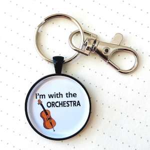 May include: A round keychain with a black border, featuring the text "I'm with the ORCHESTRA" and a cartoon violin. The keychain has a silver keyring and a lobster clasp.
