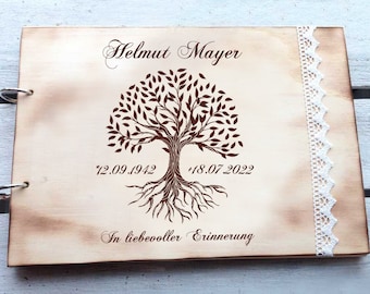May include: A wooden photo album with a tree of life design, the name "Helmut Mayer" and the dates "*12.09.1942  †18.07.2022" engraved on the front. The album has a white lace trim and the words "In liebevoller Erinnerung" are also engraved on the front.