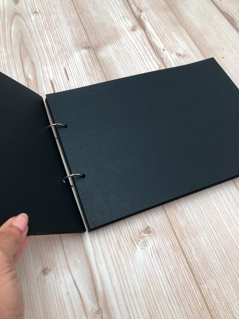 May include: A black photo album with a ring binding system. The album is open to reveal blank pages.