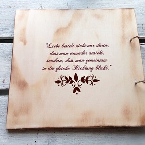 May include: A wooden photo album with a quote about love and looking in the same direction. The quote is in German and reads "Liebe besteht nicht nur darin, dass man einander ansieht, sondern, dass man gemeinsam in die gleiche Richtung blickt."