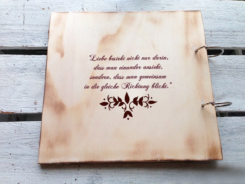 May include: A wooden photo album with a quote about love and looking in the same direction. The quote is in German and reads "Liebe besteht nicht nur darin, dass man einander ansieht, sondern, dass man gemeinsam in die gleiche Richtung blickt."