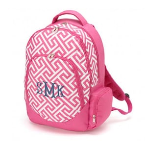 May include: A bright pink backpack featuring a white geometric Greek key pattern on the main compartment and front pocket. The front pocket displays the embroidered navy blue monogram letters SMK. It includes a top handle and side pockets.
