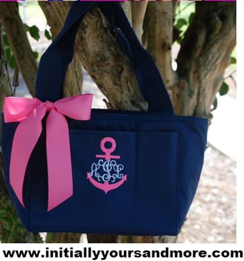 May include: A navy blue tote bag with a pink bow and an embroidered anchor with a monogram. The bag has a zippered pocket and a large pocket on the front.