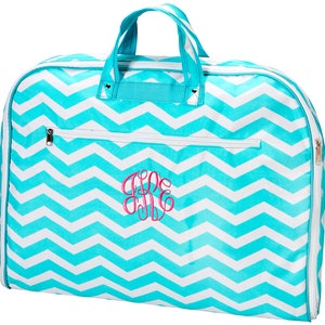 May include: A turquoise and white chevron patterned garment bag with a zipper closure and a pink monogrammed initial in the center.