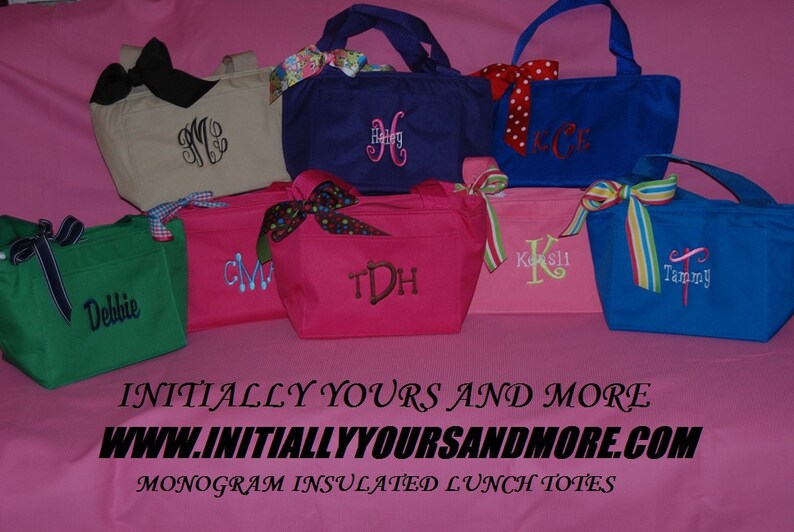 May include: A collection of eight personalized insulated lunch totes in various colors, including green, pink, blue, and beige. Each tote features a different embroidered monogram, such as "CM", "Debbie", "TDH", "Kosli", and "Tammy". The totes are displayed on a pink surface with the text "INITIALLY YOURS AND MORE WWW.INITIALLYYOURSANDMORE.COM MONOGRAM INSULATED LUNCH TOTES".