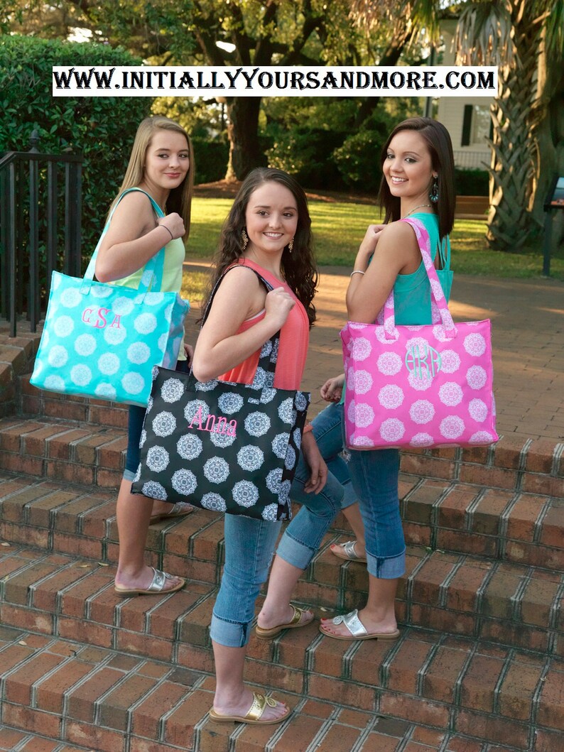 Puede incluir: Tres mujeres est&aacute;n de pie en una escalera de ladrillo, cada una llevando un bolso de mano con un dise&ntilde;o monogramado. Las bolsas son de diferentes colores y patrones, incluyendo turquesa con lunares blancos, negro con dise&ntilde;os florales blancos y rosa con dise&ntilde;os florales blancos. El texto en las bolsas dice "G.S.A", "Anna" y "G.S.A".