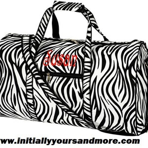 May include: Black and white zebra print duffel bag with a zippered pocket and a black zipper pull. The bag has a black handle and a black adjustable shoulder strap. The bag is personalized with the name "Susan" in red embroidery.