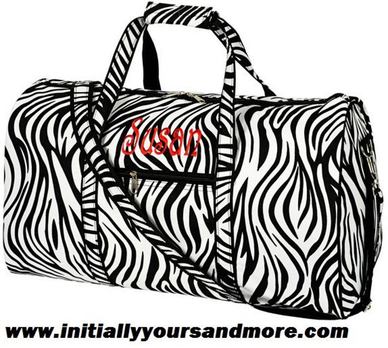 May include: Black and white zebra print duffel bag with a zippered pocket and a black zipper pull. The bag has a black handle and a black adjustable shoulder strap. The bag is personalized with the name "Susan" in red embroidery.