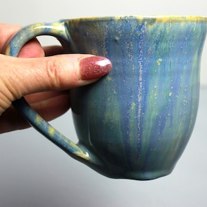 May include: A blue and yellow ceramic mug with a speckled glaze. The mug has a handle and is handmade.