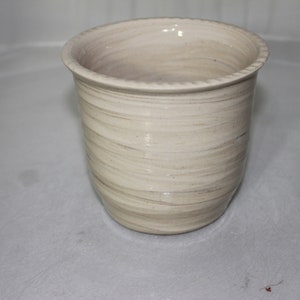 May include: A white ceramic planter with a swirl pattern. The planter is empty and has a smooth, glazed finish.