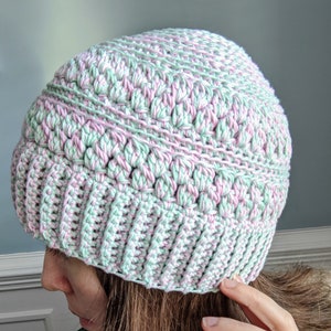 May include: A handmade crochet hat in a soft color palette of mint green and pale pink. The hat features a ribbed brim and a textured stitch pattern on the crown. This cozy winter hat is perfect for adding a touch of handmade charm to any outfit.