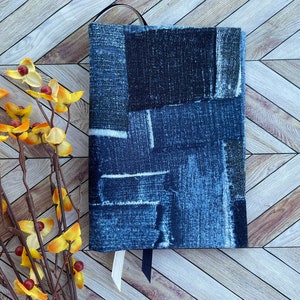 May include: A blue denim book cover with a patchwork design. The cover is made of different pieces of denim fabric sewn together.