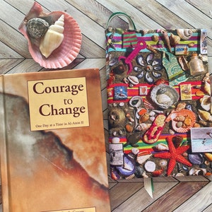 May include: A book titled "Courage to Change: One Day at a Time in Al-Anon II" with a colorful book cover featuring a variety of seashells, starfish, and other beach-themed items.