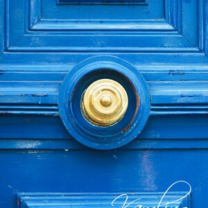 Puede incluir: Un primer plano de un llamador de puerta de latón en una puerta de madera azul brillante. El llamador es circular con un diseño de anillos concéntricos.