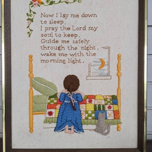 May include: Embroidered framed artwork featuring a girl in a blue dress praying by her bed. The text reads "Now I lay me down to sleep, I pray the Lord my soul to keep. Guide me safely through the night, wake me with the morning light."