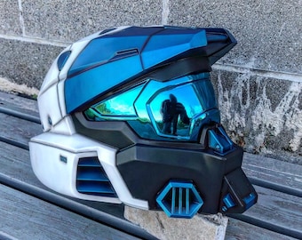 May include: A white and blue helmet with a visor. The helmet has a futuristic design and is made of plastic. The visor is tinted blue and reflects the surrounding environment.