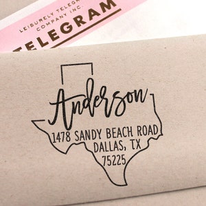 May include: A black and white rubber stamp with the text "Anderson" in a cursive font. The stamp also includes a graphic of the state of Texas with the address "1478 Sandy Beach Road, Dallas, TX 75225".