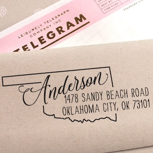 May include: A brown paper envelope with a black and white rubber stamp. The stamp features the name "Anderson" in cursive script, the address "1478 Sandy Beach Road, Oklahoma City, OK 73101", and an outline of the state of Oklahoma.
