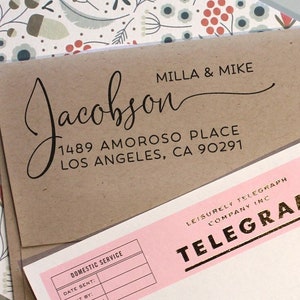 May include: A brown paper envelope with a black ink return address that reads "MILLA & MIKE Jacobson 1489 AMOROSO PLACE LOS ANGELES, CA 90291". The envelope is partially covering a pink telegram form with gold lettering that reads "LEISURELY TELEGRAPH COMPANY INC TELEGRAM".