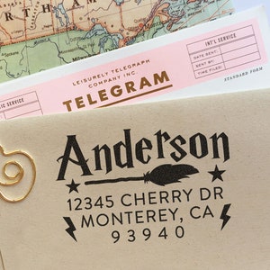 May include: A gold-colored paper clip in a cloud design rests on a tan envelope with the name "Anderson" and address details printed in black. A pink telegram and a vintage map are in the background.