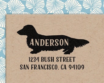 May include: A tan card features a black silhouette of a dachshund with the name "ANDERSON" printed across its body. Below, the address "1234 BUSH STREET SAN FRANCISCO, CA 94109" is printed in black. The background has a blue and white leaf pattern.