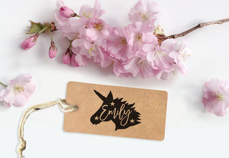 May include: A brown paper tag with a black silhouette of a unicorn's head and the name "Emily" written in a cursive font. The tag is tied with a white string and surrounded by pink cherry blossoms.