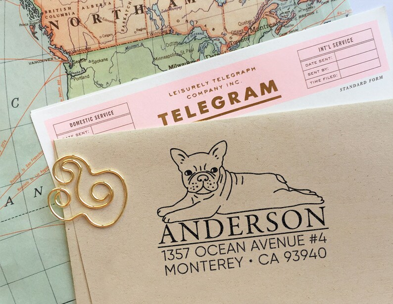 K&ouml;nnte beinhalten: Ein brauner Umschlag mit einer goldenen B&uuml;roklammer und einem schwarzen und wei&szlig;en Stempel eines franz&ouml;sischen Bulldoggen mit dem Text "Anderson 1357 Ocean Avenue #4 Monterey CA 93940".
