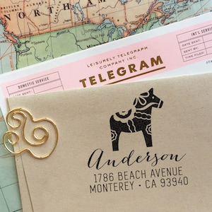May include: A brown envelope with a gold paper clip. The envelope has a black and white rubber stamp of a Dala horse with the text "Anderson 1786 Beach Avenue Monterey CA 93940".