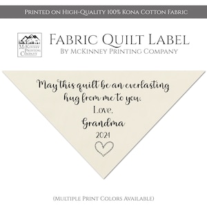 May include: A beige triangle-shaped fabric quilt label with black text that reads "May this quilt be an everlasting hug from me to you. Love, Grandma 2024" with a small black heart below the text. The label is printed on high-quality 100% Kona cotton fabric.