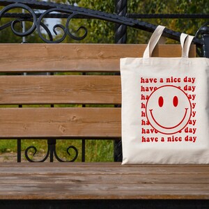 May include: A white tote bag with a red smiley face and the text "have a nice day" repeated multiple times.