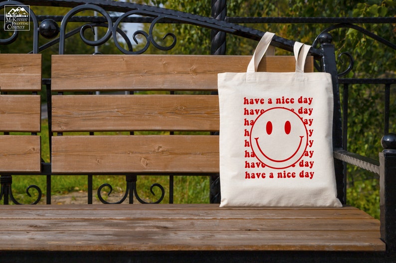May include: A white tote bag with a red smiley face and the text "have a nice day" repeated multiple times.