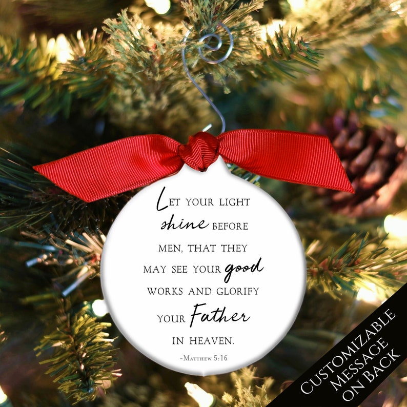 May include: White round Christmas ornament with a red ribbon. The ornament features a black and white quote from Matthew 5:16, "Let your light shine before men, that they may see your good works and glorify your Father in heaven."