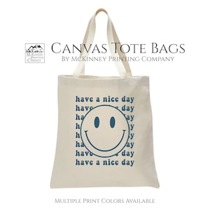 May include: A white canvas tote bag with a blue smiley face and the text "have a nice day" repeated multiple times. The bag is made by McKinney Printing Company.
