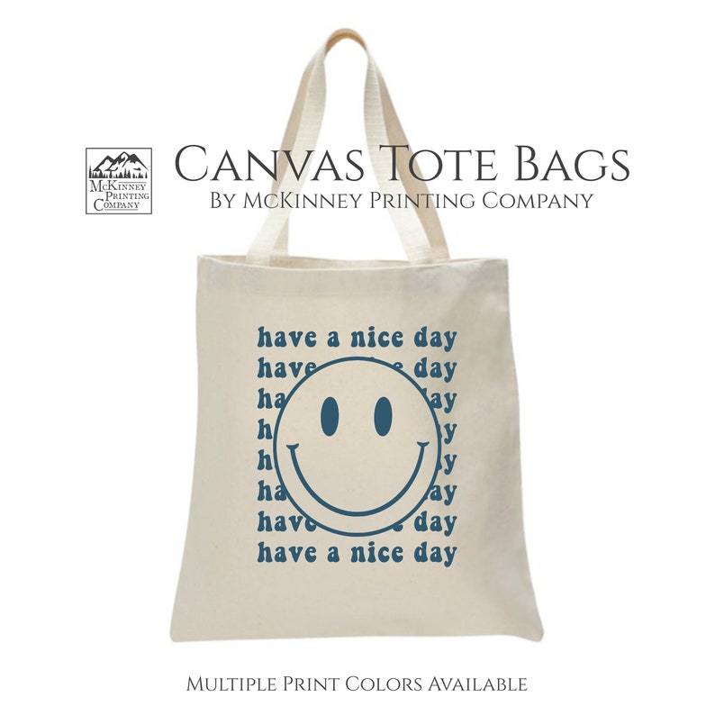 May include: A white canvas tote bag with a blue smiley face and the text "have a nice day" repeated multiple times. The bag is made by McKinney Printing Company.